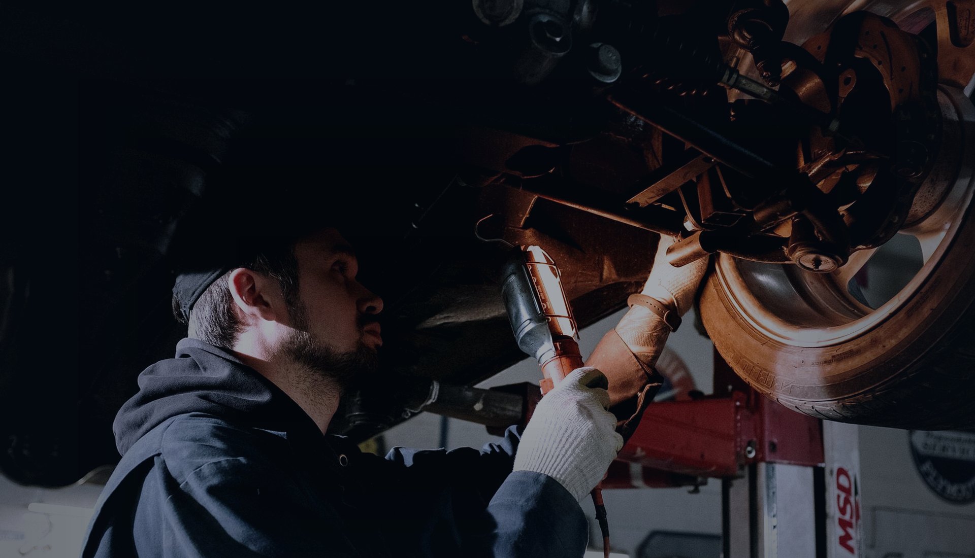 Mechanic working under a vehicle on a workshop lift with an inspection lamp