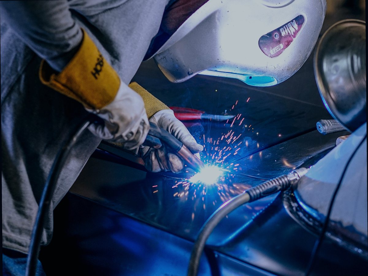 Welder in a helmet MIG welding a car body panel